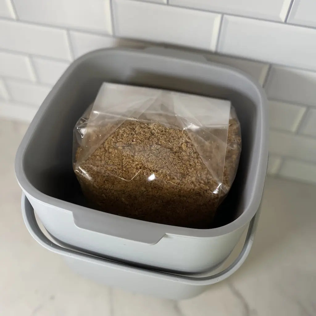 Close Up Of A 7L Grey Coloured Bokashi Bin With A 1KG Bag Of Organic Bokashi Bran Mix