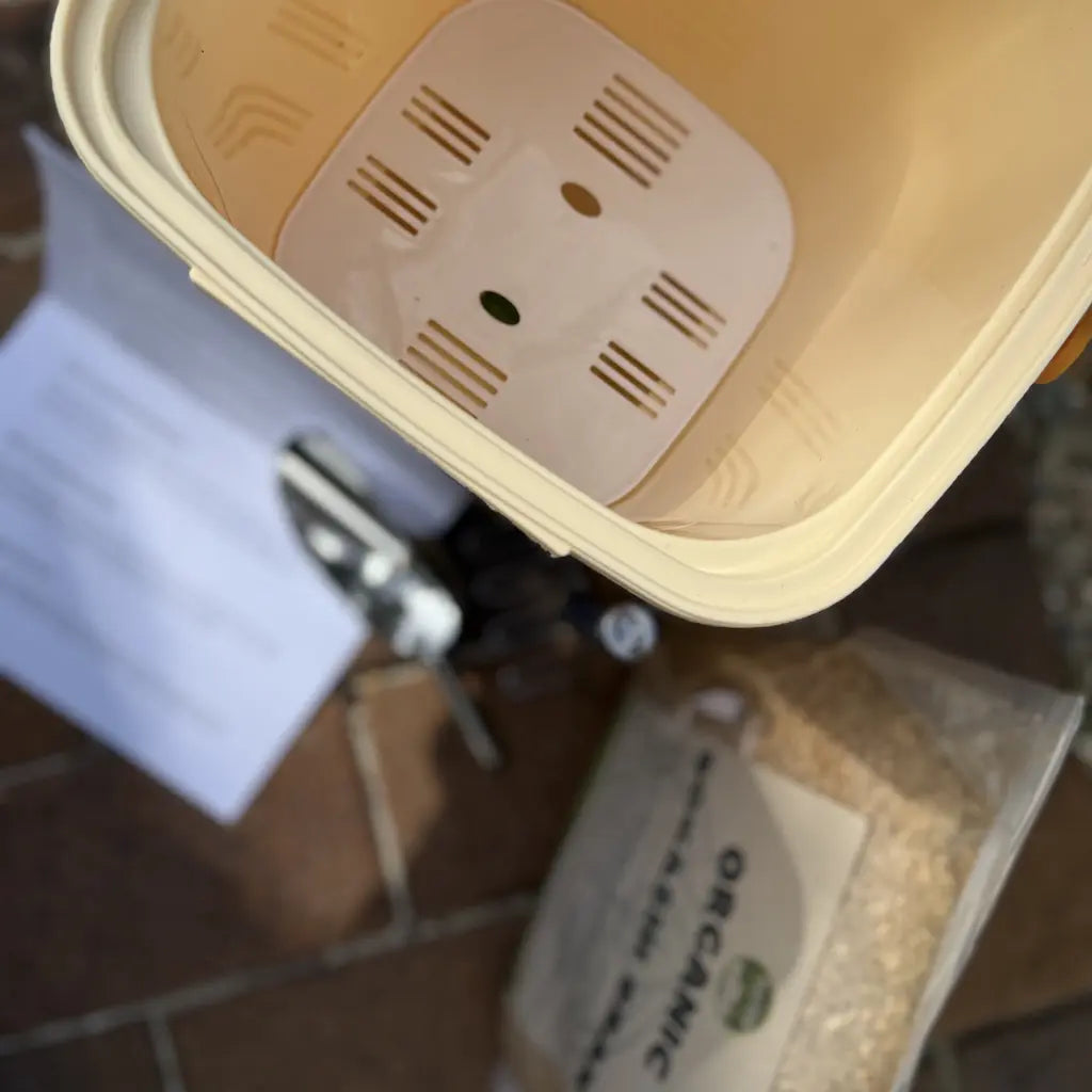 Close-up of a beige compost bin with a bag of organic bran in the foreground.