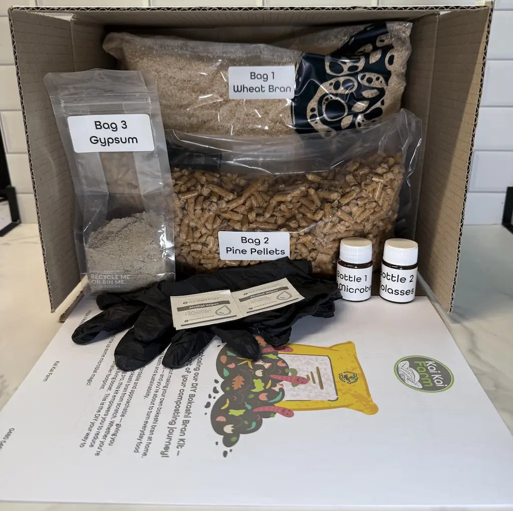 Box containing DIY Bokashi bran kit supplies including bags of wheat bran, pine pellets, and bottles containing 'EM-1 Microbes' and 'Molasses'.
