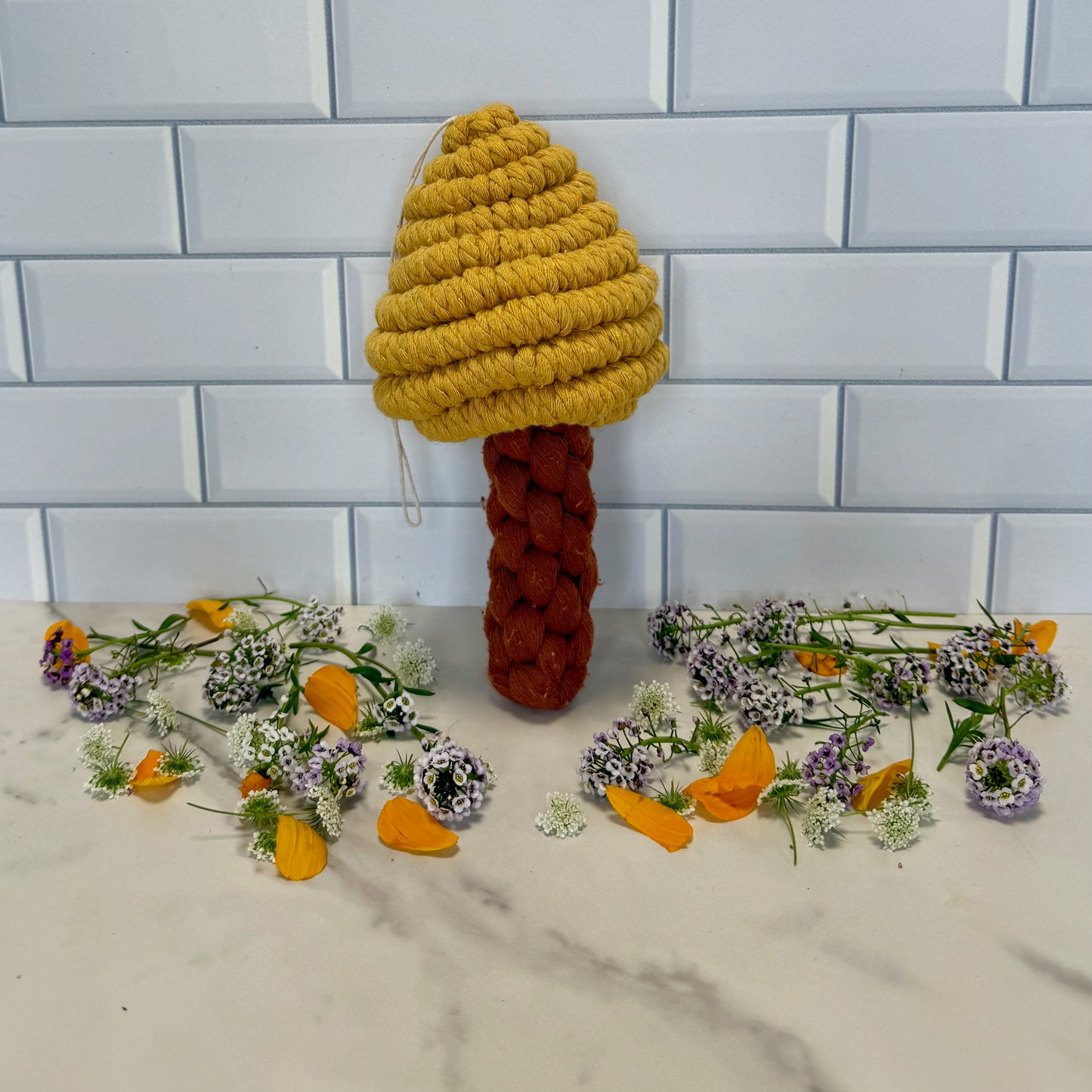 Knitted macrame mushroom on a table with flowers and leaves.