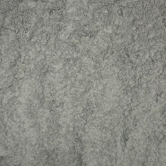 A pile of fine, grayish mineral rock dust spread on a white surface, showing its powdery texture and natural composition