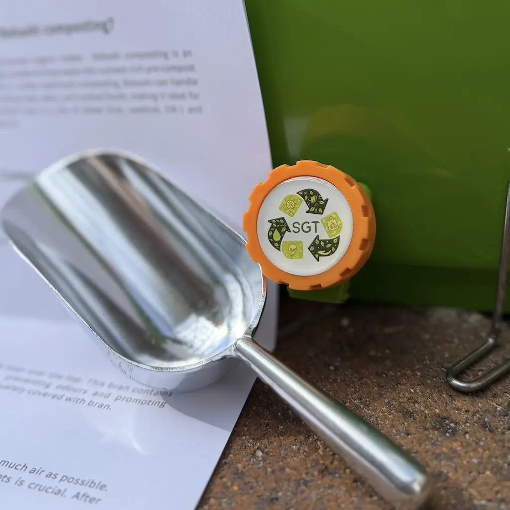 Metal scoop for measuring Bokashi bran next to the 20L Bokashi bin tap