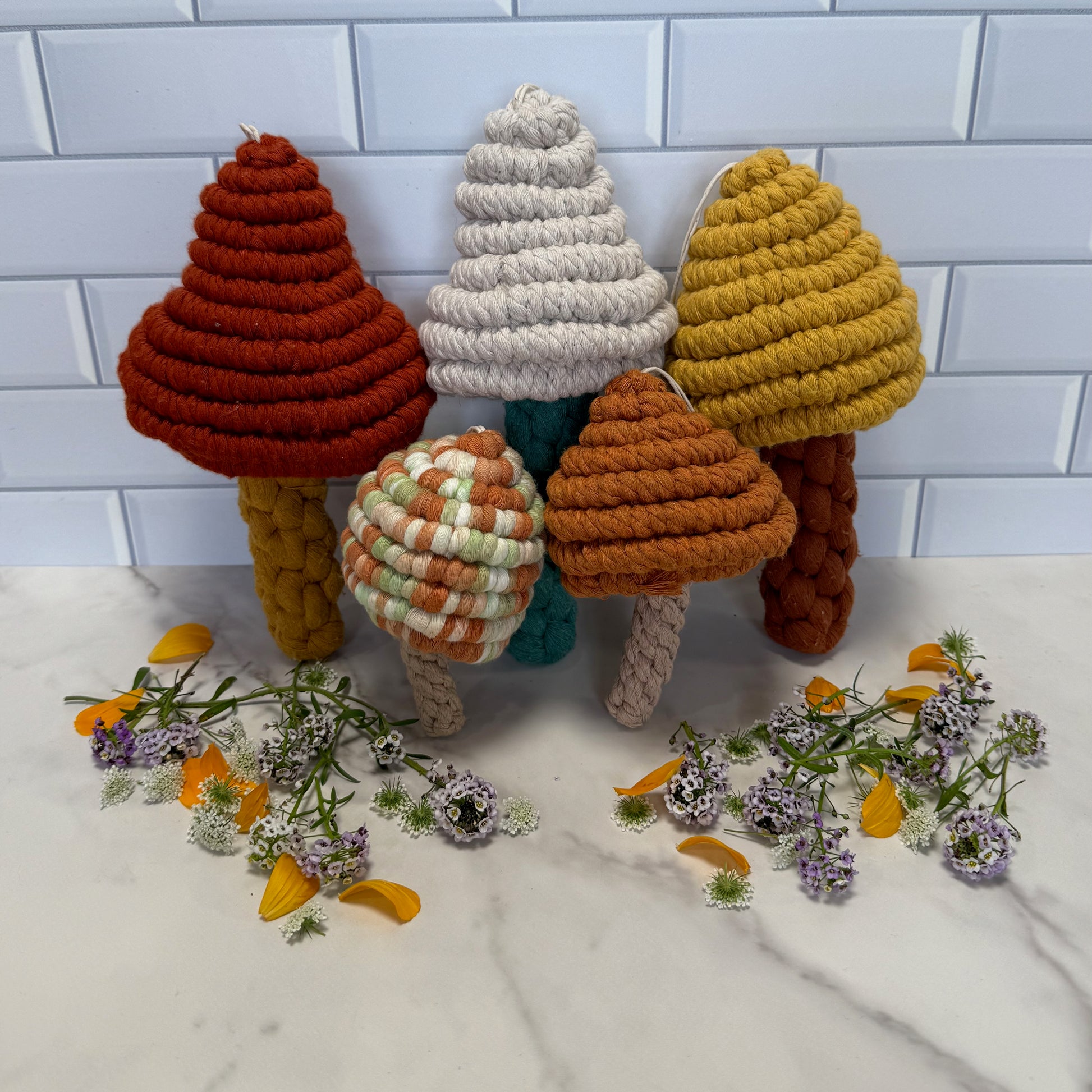 Colourful knitted macrame mushrooms on a white surface with flowers.