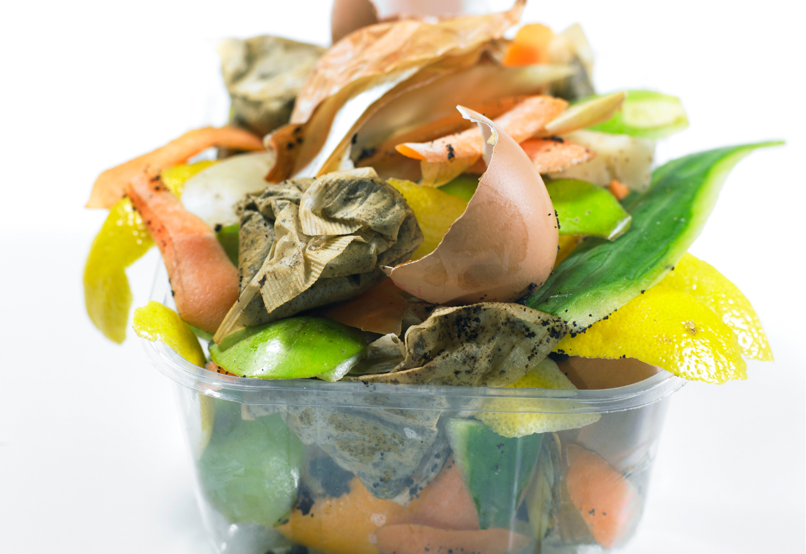 Clear container filled with various food scraps including vegetables and leaves ready for Bokashi bin