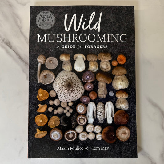 Book cover of 'Wild Mushrooming: A Guide for Foragers' with mushroom illustrations on a dark background.